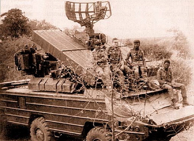 На броне боевой машины ПВО «ОСА-АК» инженер Брянского автозавода А. Павлов (второй слева). Снимок сделан после успешного отражения налёта южноафриканской авиации на позиции ФАПЛА. Район Риу-де-Арея и Шибембы, 1985 г.