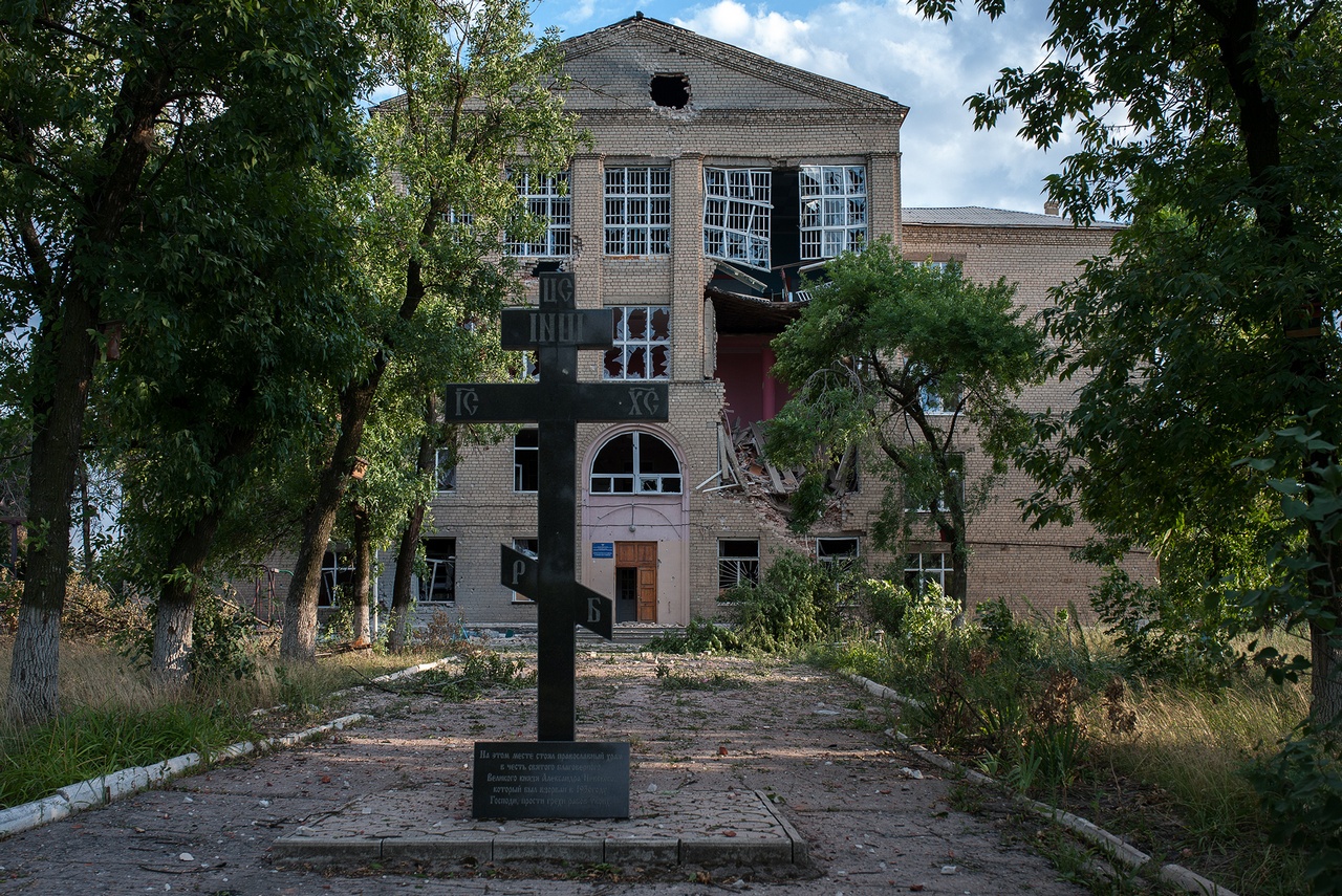 Крест перед разбитым зданием школы чудом уцелел.